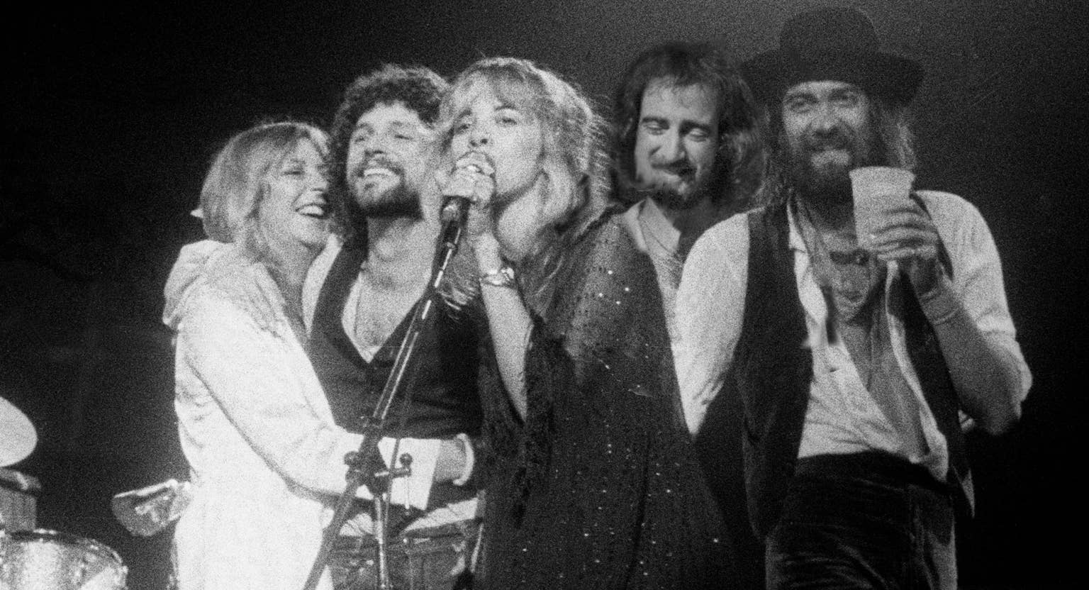 A Fleetwood Mac tagjai együtt a színpadon, Stevie Nicks a mikrofon mögött.